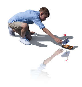 cut out boy playing with a toy boat by the water
