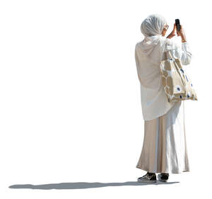 muslim woman in a white outfit taking pictures with her phone