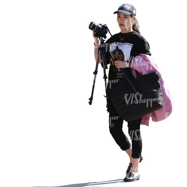 backlit asian woman walking and carrying a camera and tripod