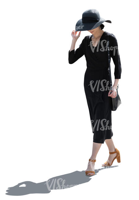 backlit asian woman in a black dress and wearing a black hat walking