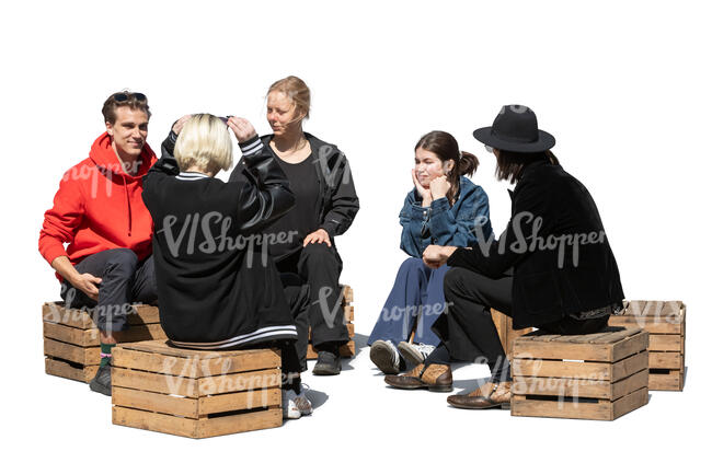 group of young people sitting on wooden boxes outside and talking
